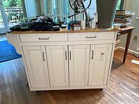 Front view of white kitchen island showing butcher block top, drawers and cabinet doors