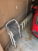 Photo of white folding step stool with black steps and a piece of cloth draped over it, set against a wooden background near a red car.