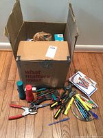 Photo of cardboard box with assorted hand tools, flashlights, pens, and coasters visible on floor