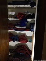 Closet shelves with folded linens including towels, blankets, sheets, and rolls of toilet paper