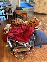 Wide view of lot items including stacked cushions, pillows, storage basket, and large stuffed tiger plush on floor.