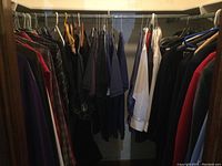 View of men's clothing items hung on hangers showing variety of jackets, shirts, and pants in a closet.