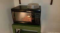 Black Kenmore microwave oven sitting on green table with plastic container on top.