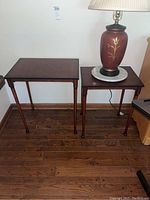 Two wooden nesting tables side by side on a hardwood floor, a lamp rests on the smaller table.