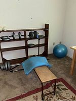 Overall view of weight bench, shelf with weights, yoga ball and yoga mat on carpeted floor