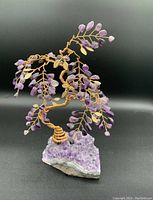 Front side view of copper wire tree with amethyst leaves on amethyst geode base, black background.