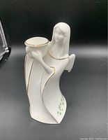 Front view of the white porcelain angel figurine holding a candle holder, showing delicate gold trim and green clovers on base.