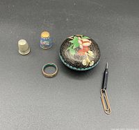 Two metal thimbles, a decorative ring, a round cloisonné trinket box with floral design, and two miniature screwdrivers on black background.