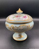 Front view of the covered candy dish showing gold lattice patterns, floral motif on lid, and gold accents on pedestal base.