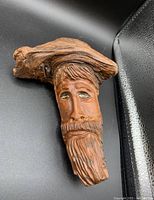 Carved wooden face ornament showing detailed facial features with carved beard and hat.