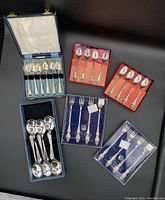Collection of seven sets of silver plated collectible spoons and forks, some in original boxes displayed on table.