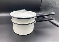 Three white enamel pots stacked, one with a lid, showing the black rims and handles.