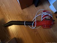 Red Craftsman electric leaf blower with long black nozzle on wooden floor.