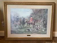 Front view of framed hunting scene with riders on horses and hunting dogs in a wooded setting, showing frame and glass.