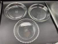 Three glass pie plates displayed on black surface, two with smooth edges and one scalloped edge plate.