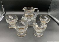 Photo of the glass ice tea jug and four cups showing gold trim and floral design, arranged in a set.