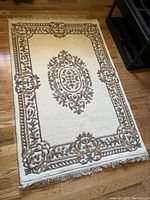 Full view of cream-colored rectangular rug with floral borders and central medallion pattern placed on hardwood floor.