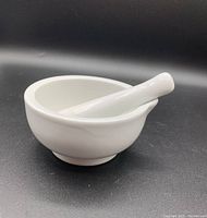 Side view of white ceramic mortar and pestle set on black background showing mortar bowl and pestle resting inside.