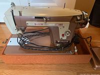 Photo of the Piedmont sewing machine mounted on a metal base plate, cream-colored with control knobs and dials, showing the motor attached.