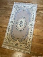Full view of rectangular area rug on wood floor showing overall design, colors, and fringed edges