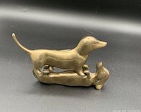 Two bronze dachshund dog figurines on a black background, one standing and one lying on its back.