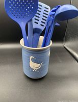 Blue pottery utensil holder with white bird design and blue plastic kitchen utensils inside.