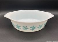 Front view of white Pyrex casserole dish with blue-green snowflake decoration around the sides, showing handles on either side.