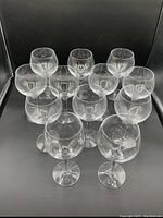 Twelve clear glass wine glasses arranged in a group on a black surface.