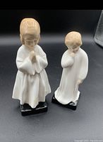 Photo showing two Royal Doulton porcelain figurines, Darling and Bedtime, in white nightgowns with beige hair on black bases against a black background.