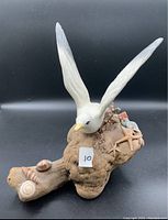 Front view showing the white seagull figurine with wings extended perched on the driftwood base decorated with seashells and a starfish.