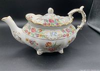 Side view of the porcelain tea pot showing floral pattern, spout, and ornate handle with gold accents.