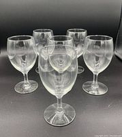 Front view of six clear stemmed white wine glasses arranged on black background, showing rounded bowls and sturdy bases.