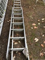 12 foot aluminium straight ladder laying on ground, showing side and rungs with some dirt and wear.