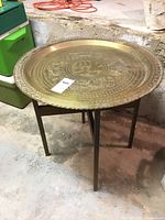 Side view of the Asian brass plaque table showing its round top and wood frame with four legs