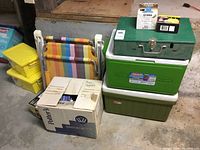 Overview of total items including two folding chairs, cardboard picnic supply box, yellow storage boxes, and coolers with metal box stacked.