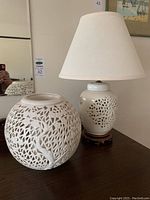 Photo showing both the candle holder and lamp side by side on surface, highlighting their white ceramic botanical cut-out designs.