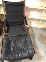 Full view of the black canvas chair with wooden frame and tufted black leather ottoman in front.