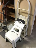 Whole lot showing the hand truck leaning against the wall with three step stools stacked in front.