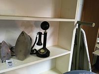 Small vintage travel iron with green handle displayed on white shelf