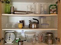 Full view of kitchenware inside cabinet shelves showing various containers, kettle, ramekins, and pitchers.