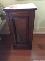 Front view of antique small wooden cabinet with framed panel door and brass pull tab handle.