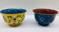 Two painted Chinese porcelain bowls, one yellow with blue interior, the other blue with red interior, showing floral designs and craftsmanship.