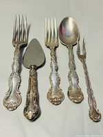 Five vintage Birks Regency Plate flatware pieces arranged side by side including forks, spoon, cake server with ornate handles.