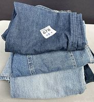 Three pairs of folded denim pants stacked showing varying shades of blue denim, all size 32+