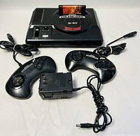 Front angled view of SEGA Genesis console with The Lion King game in slot, two wired controllers, and power supply.