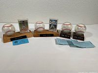 Four autographed baseballs with protective cases, wooden stands, name plaques, player cards, and certificates of authenticity arranged in a row.