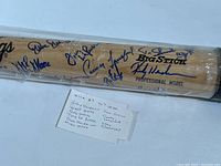 Full-length view of Rawlings Big Stick bat in plastic wrap showing multiple blue-ink signatures