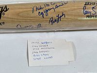 Close-up image of bat signatures, showing blue ink autographs with a handwritten note listing some names.
