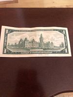Back side of 1967 Canadian Centennial one dollar bill showing Parliament buildings and bilingual centennial text.