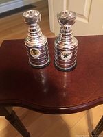 Photo shows two silver mini Stanley Cup trophies sitting on a wooden table. On the left is the trophy with a Chicago Blackhawks logo. On the right is the trophy with a Dallas Stars logo.